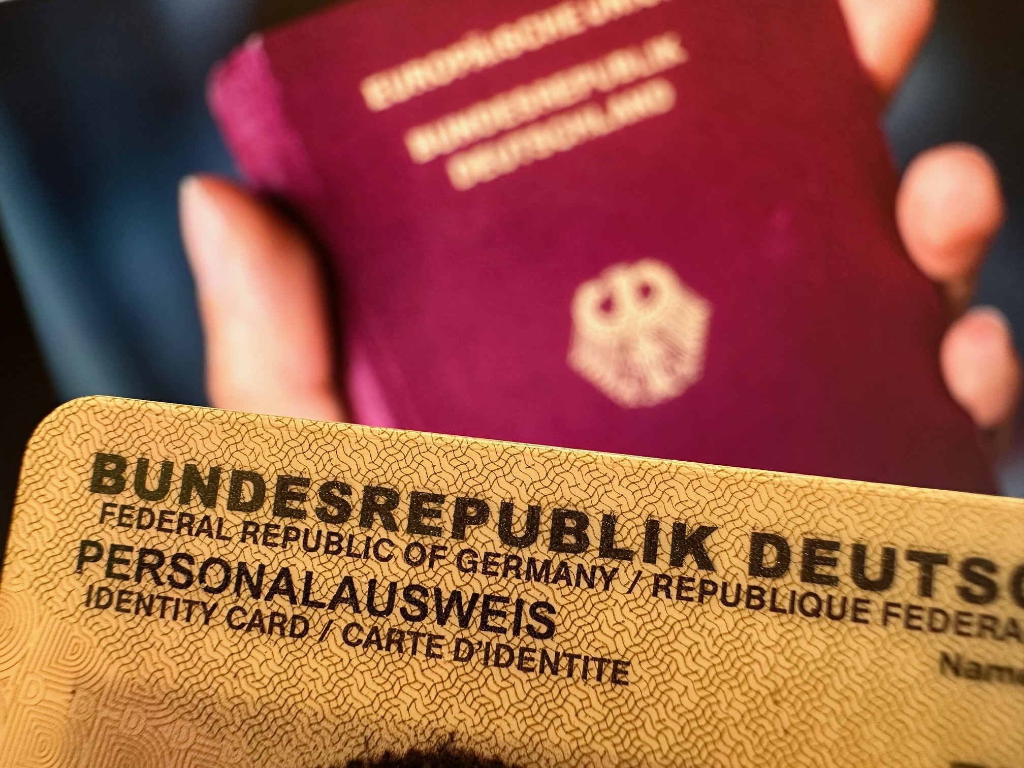 Bild eines Personalausweises - im Hintergrund unscharf ein Reisepass mit dem Bundesadler