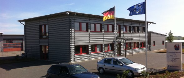 Graues Flachdachgebäude des Technischen Dienstleistungszentrums mit Flaggen vor der Eingangstür