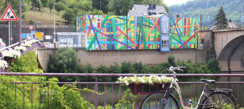 grafisch bunt gestaltete Außenansicht des Gebäudes der Deutsch-Luxemburgische Tourist-Information mit Fahrrad im Vordergrund